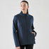 A woman wearing a navy softshell jacket with a high collar and side pockets, featuring a logo on the sleeve.