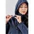 A woman adjusts the fastening on a navy lightweight rain jacket with a hood, featuring a logo on the sleeve.