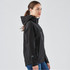 A women's black softshell jacket with a hood, featuring zippered pockets and a fitted silhouette.