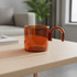 An amber glass tea and coffee cup with a distinctive handle, placed on a wooden table.