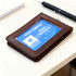 A brown leather ID card holder featuring a clear slot for identification and a pen on a desk.