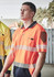 Men's short sleeve polo in high visibility orange with segmented reflective tape and a logo on the chest.