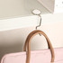 A round, curved metal desk hook in silver holds a pink bag on the edge of a white desk.