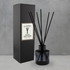 A round black glass reed diffuser with five black reeds, displayed beside a black box featuring a logo.