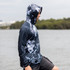 A men's polyester sublimated 1/4 zip fishing hoodie in dark blue with a graphic pattern, worn by a person by the water.