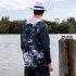 A men's polyester sublimated 1/4 zip fishing hoodie in navy and grey, featuring a hood and a logo, worn by a person by the water.