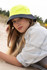 A luminescent yellow and navy bucket hat resting on sand, worn by a person with long hair. The setting appears outdoors.