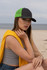A cap featuring a black front and a vibrant green mesh back, worn by a model on a beach.