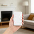 A hand holding a white 5000mAh magnetic wireless power bank in a home setting with a fireplace and sofa in the background.