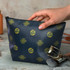 A medium navy cosmetic bag with gold patterns, featuring a hand reaching for it, alongside makeup brushes.