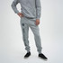A model wearing grey unisex sweatpants with a logo and text along the side, paired with black shoes.