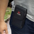 A black phone pouch with a logo, featuring a secure flap and designed for attaching to a belt or waistband.