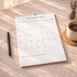 A vertical wall calendar for September 2026, featuring a clean white design, placed on a table with a coffee mug and pen.