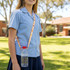 A drink bottle sling lanyard in a light orange pattern, holding a clear water bottle, worn by a student outdoors.