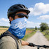 A cyclist wearing a blue UPF 50+ perforated ice silk neck gaiter featuring mountain designs against a rural backdrop.