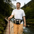 A drink bottle holder waist bag in grey and black, being worn by a man on a wooden bridge in a forested area.