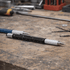 A black and silver precision pen lies on a workbench, surrounded by tools and small metal parts.