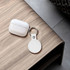 A white tracking tag with a keyring attached, beside a white protective case, on a wooden surface.