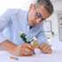 A man with glasses uses a green pipe wrench-shaped ballpoint pen while drawing on paper.