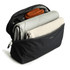 A black packing cube filled with a grey blanket, a beige item, and an orange accessory, featuring a mesh panel on top.