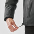 A hand adjusting the hem of a men's thermal jacket in a dark colour, featuring a logo on its side.