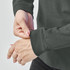 A close-up of a person adjusting the cuff of a dark green long-sleeve t-shirt featuring a logo.