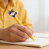 A yellow pen with a cute black and white cat design on the top, held in a person's hand over a notebook.
