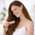 A woman with long hair holds a pink comb, smiling gently in a bright, softly lit setting.