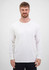A man wearing a plain white long sleeve tee stands against a neutral background. The tee has a brand logo.