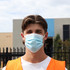 A cloth face mask in light blue worn by a young man, who is also wearing a bright orange vest.