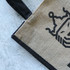 A jute tote bag in natural and black colours featuring a simple design and sturdy handles.
