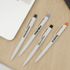 A collection of white plastic pens in black, orange, and blue with various logos on a wooden surface.