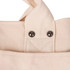 Close-up of a cream canvas tote bag featuring textured fabric and metal studs on the strap attachment.