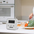 A digital kitchen timer in white with a large display, placed on a kitchen countertop beside fresh vegetables.