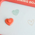 A red magnetic drawing board featuring a textured surface and a heart-shaped magnetic stamp in orange.