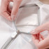 A mesh laundry bag with a zippered opening, featuring a white colour and grey accents. Hands are shown holding the zipper.