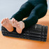 A black foam massage roller rests on a surface, with a person’s bare feet placed on top.