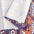 A small table runner featuring a vibrant pattern in orange and navy, with a prominent logo and neat stitching.