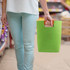 A green felt tote bag is held by a person wearing light blue pants, with a distinctive handle. The bag has a logo.