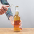 A drink bottle opener shaped like a wrench in silver, held by a hand over a beer bottle on a wooden surface.