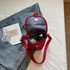 A small red canvas shoulder bag with a grey interior, featuring a flap and strap, containing drink bottles.