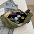 An olive green crossbody bag opened to display various items, including a drink bottle, a notebook, and makeup products.