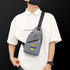 A grey sling chest bag with zippers and a logo, worn across a person's body over a white shirt.
