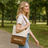 A woman walks in a park carrying a cream and brown convertible canvas backpack to tote bag with a logo.
