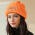 A twisted cable cuffed beanie in bright orange, featuring a logo on the front, worn by a model.