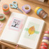 A flat lay of a notebook with a leaf and tree photo, surrounded by colourful washi tape, scissors, and a tape dispenser.