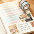 A roll of washi tape in pale blue and brown sits on an open notebook featuring pastel stripes and decorative images.