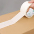 A roll of white BOPP packaging tape is being applied to a cardboard box. The tape has a logo on the backing.