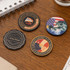 Four custom poker chips in various designs and colours, featuring logos and imagery on a wooden surface.