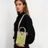 A knitted crossbody bag in yellow and blue with a handle, displayed by a model wearing a black shirt.